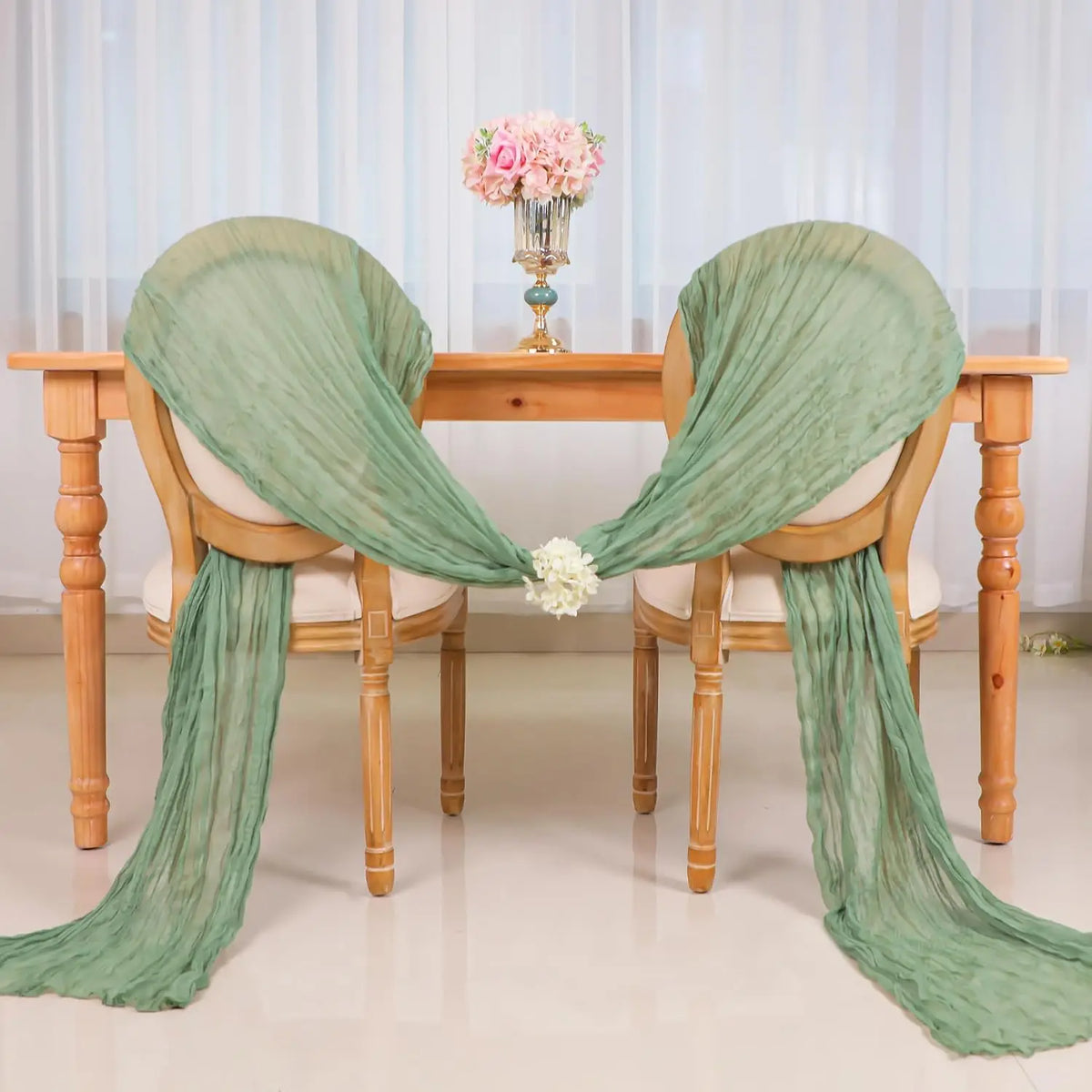 A set of ten terracotta semi-sheer cheesecloth table runners draped over wooden chairs with a pink floral centerpiece.