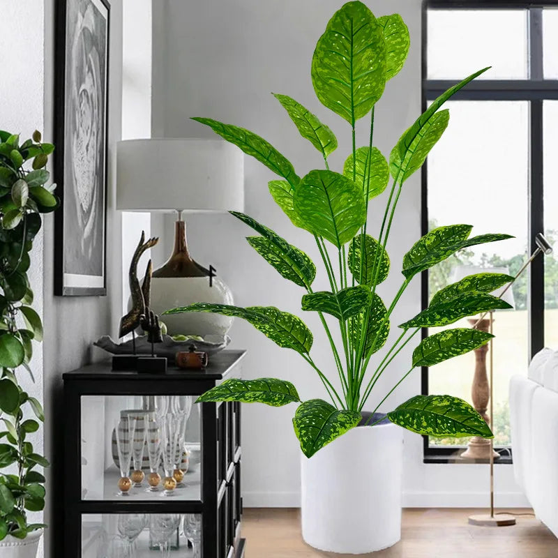 A large artificial tree with lush green leaves stands in a white pot next to a dark cabinet.