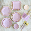 A set of pink and gold party tableware including plates, bowls, and cutlery arranged on a white surface.