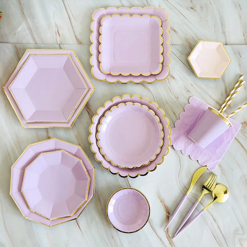 A set of pink and gold party tableware including plates, bowls, and cutlery arranged on a white surface.