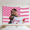 A portrait of Hyunjin making a peace sign against a pink American flag tapestry.