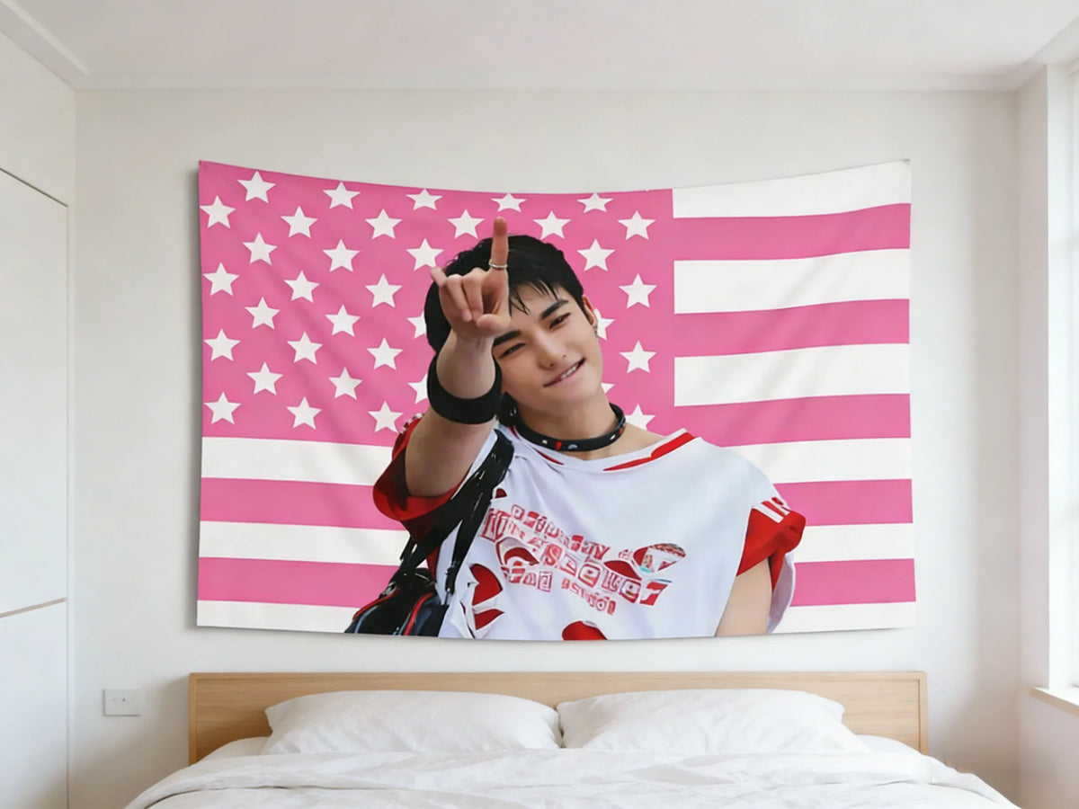 A portrait of Hyunjin making a peace sign against a pink American flag tapestry.