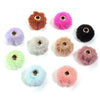 Collection de boules ou perles en peluche colorées dans les tons rose, violet, vert, beige et noir.