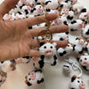 A hand holds a bunch of handmade crochet cow keychains in various white and black patterns.