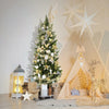 An artificial cedar topiary tree decorated with white and gold ornaments in a cozy, light-filled setting.