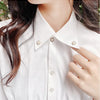 Close-up of a white collared shirt featuring pearl and rhinestone no-sew buttons.