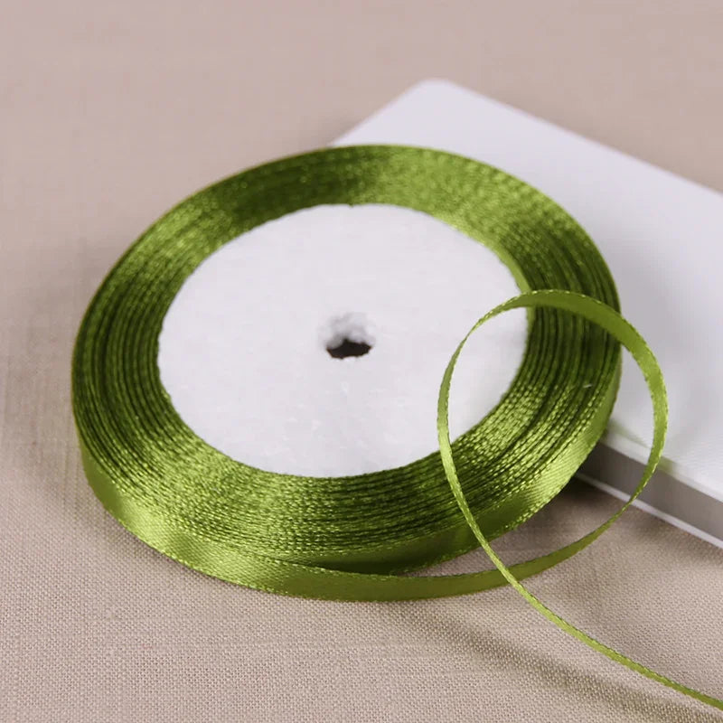 A spool of green satin ribbon for gift wrapping and DIY crafts resting on a white surface.