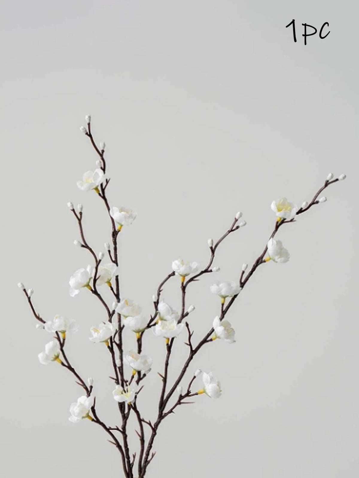 Una rama de flores blancas artificiales de ciruelo sobre un tallo oscuro contra un fondo gris claro.