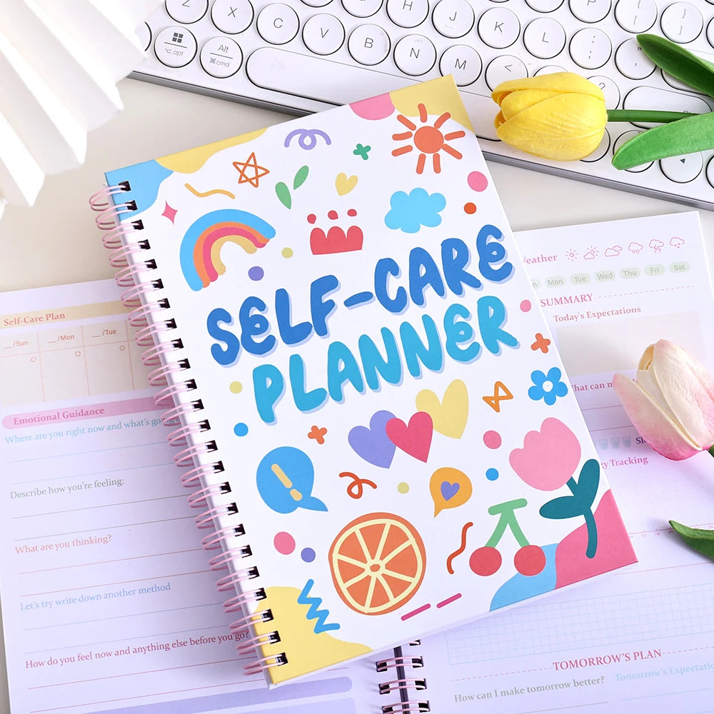 A colorful self-care planner notebook with stickers and pages is shown next to a laptop keyboard.