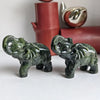 A pair of green jade elephant carvings displayed in front of a red ceramic vase.