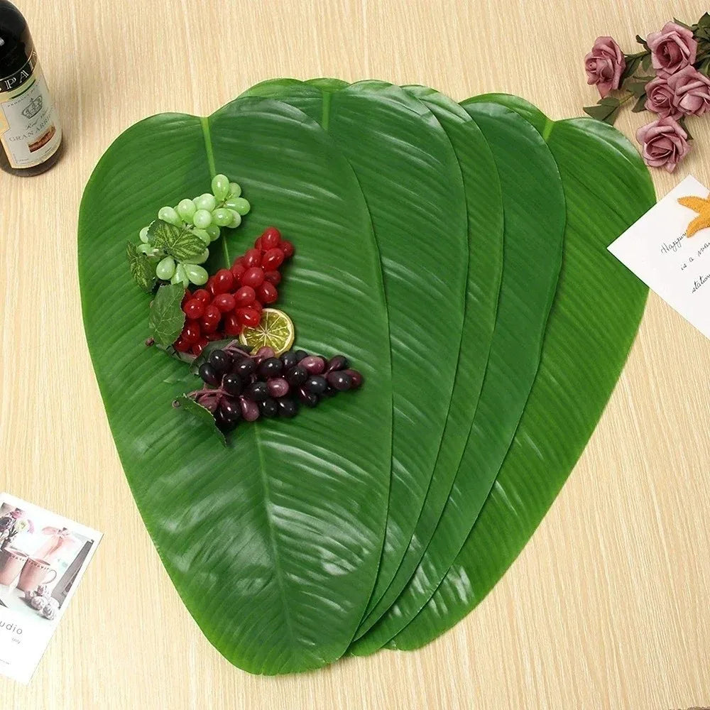 A set of five green banana leaves used as coasters, displaying various fruits and flowers on a wooden surface.