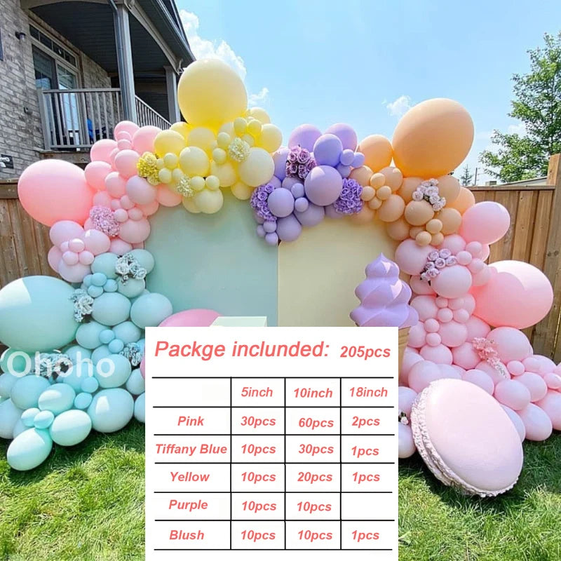 A colorful balloon garland kit featuring pink, blue, yellow, purple, and blush balloons arranged on a green lawn.