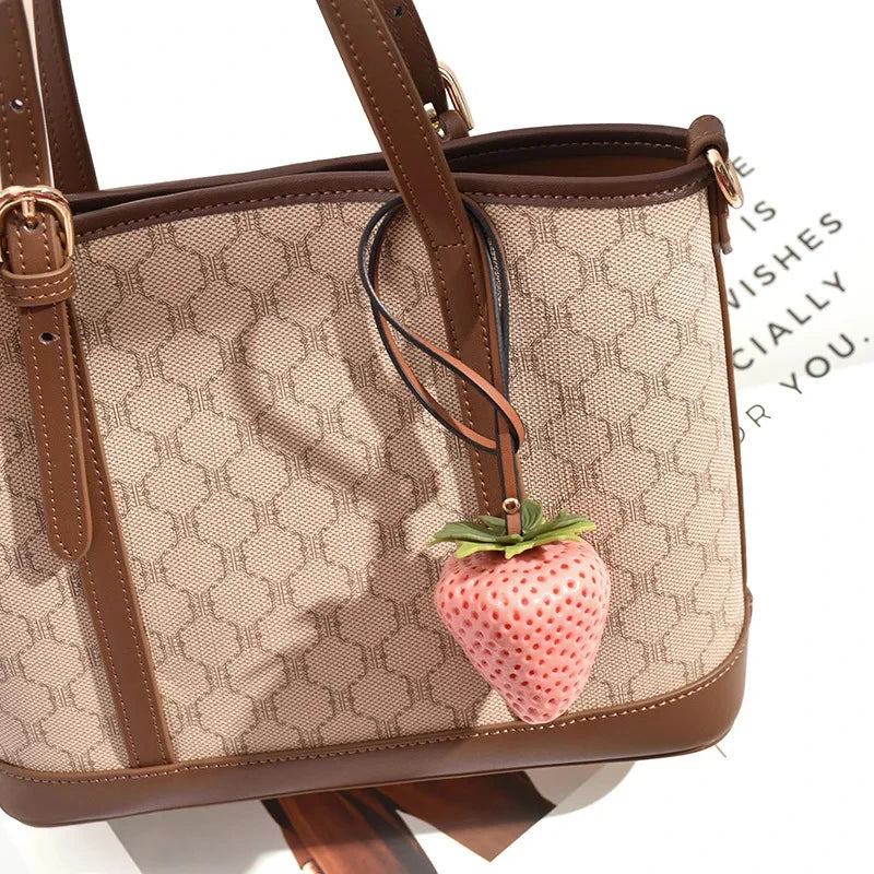 A brown quilted handbag with a tan pattern features a strawberry charm attached to the strap.