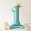 A teal foil balloon shaped like the number one with a gold crown on top.
