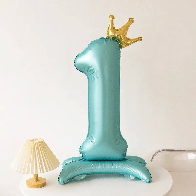 A teal foil balloon shaped like the number one with a gold crown on top.