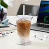 A tall plastic cup filled with iced coffee sits on a white desk next to a laptop and various office supplies.
