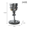 A silver mechanical piston skull sculpture with a gear base and a cylindrical top.