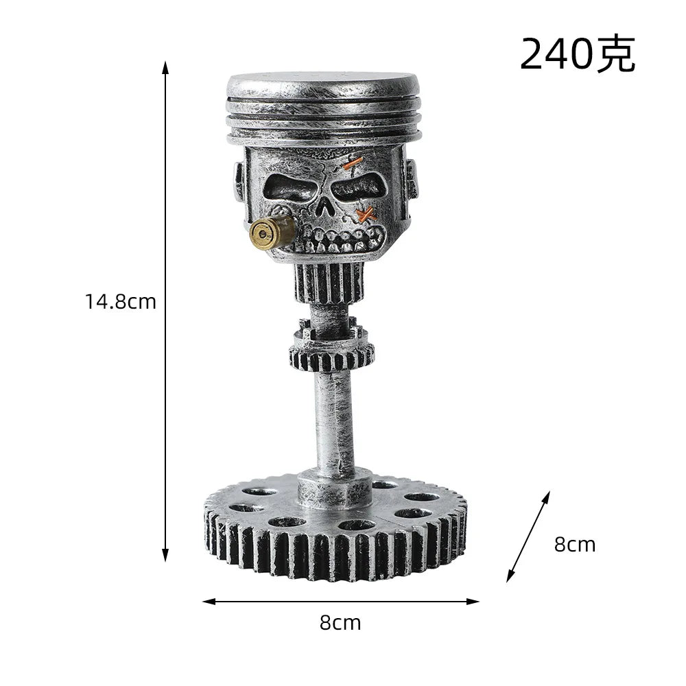 A silver mechanical piston skull sculpture with a gear base and a cylindrical top.