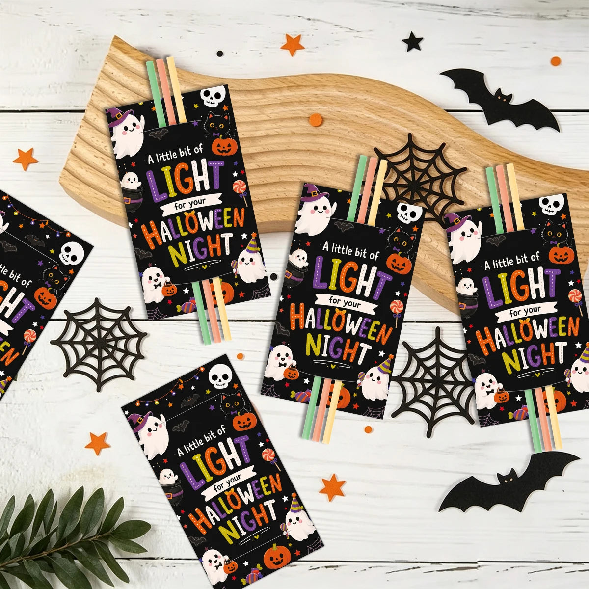 A collection of Halloween glow stick holder cards featuring bats, ghosts, and spiders arranged on a wooden board.