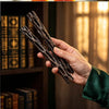 A hand holds two dark, twisted willow sticks used as a good luck gift or breakable wish box.