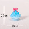A small, bright blue resin Christmas tree charm with a pink bow, resting on a white surface.
