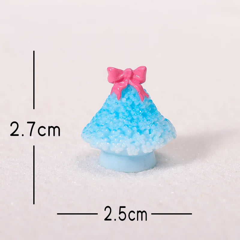 A small, bright blue resin Christmas tree charm with a pink bow, resting on a white surface.