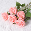 A bouquet of soft pink artificial roses with green leaves arranged on a white surface.
