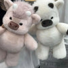 A fluffy pink Highland cow plush toy next to a white and black cow plush toy.