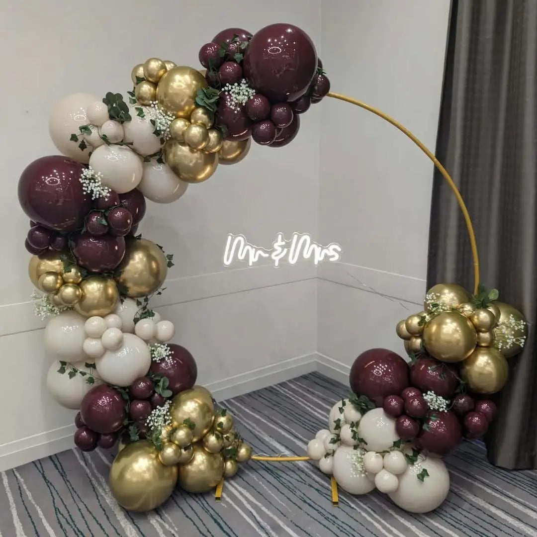 A balloon garland arch featuring burgundy, gold, and white balloons displayed against a gray background.