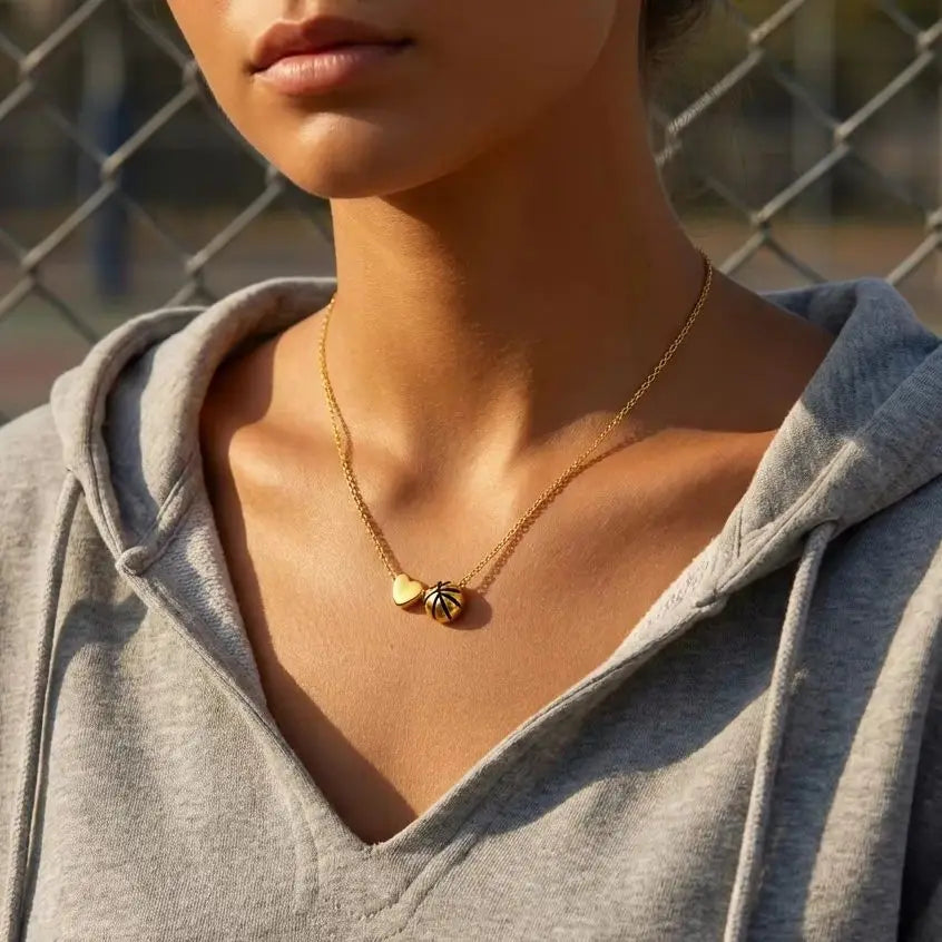 A close-up of a woman wearing a gold heart basketball pendant necklace under a gray hoodie.