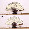A large, round decorative fan with a black and cream pattern is displayed on a wooden shelf.
