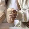 A person holds a beige tumbler with ice and foam, featuring text that reads Being my sister is really the gift you need.