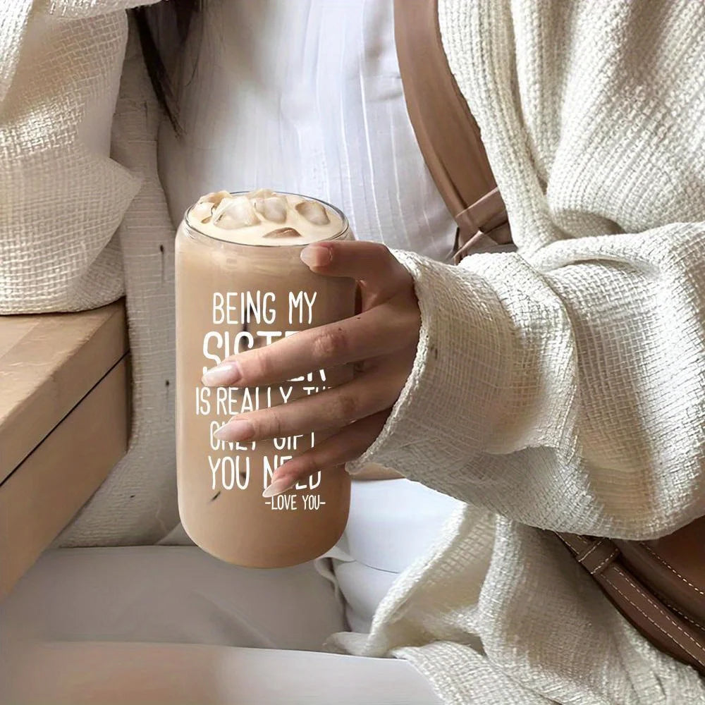 A person holds a beige tumbler with ice and foam, featuring text that reads Being my sister is really the gift you need.
