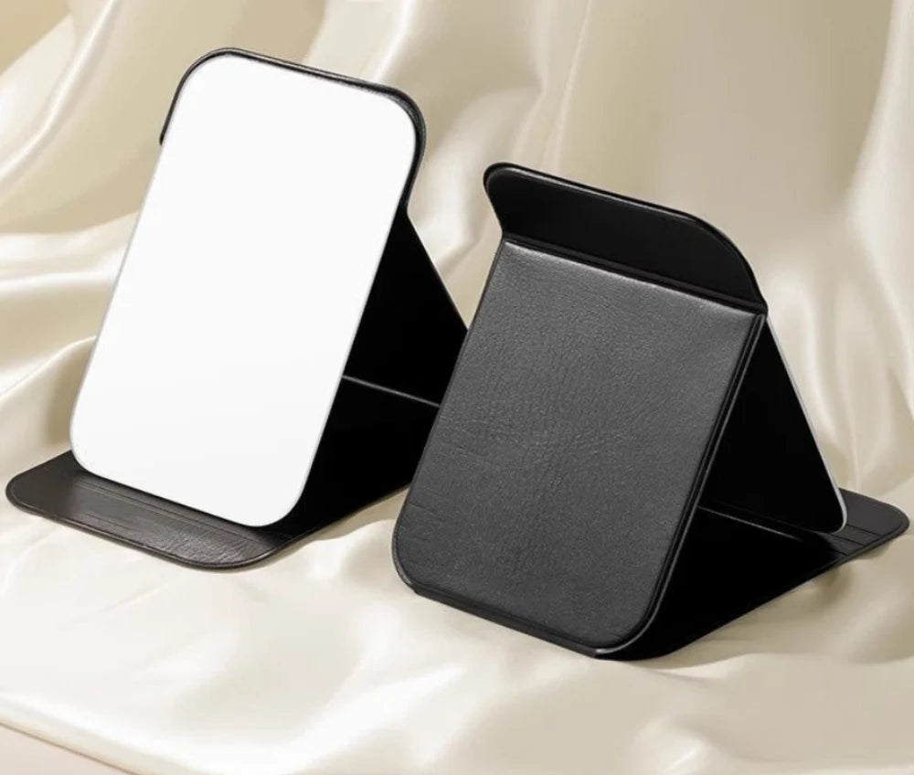 A black foldable vanity mirror with an adjustable stand is shown against a light fabric background.