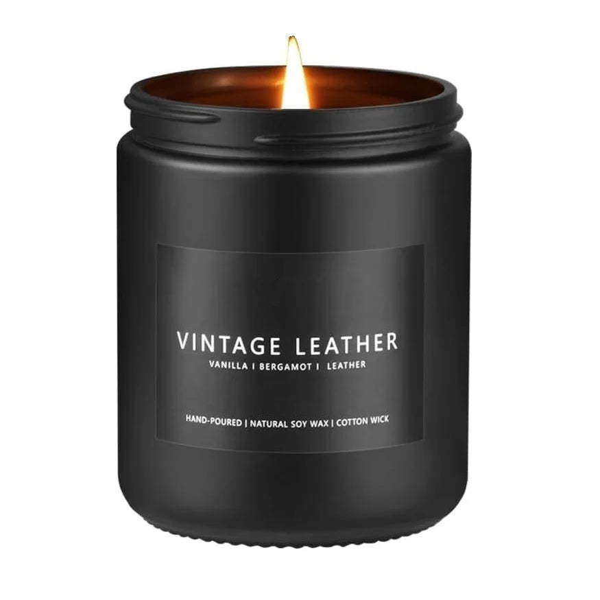 A black glass jar candle with a lit wick, labeled Vintage Leather.