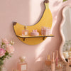 A yellow cherry-shaped wooden wall shelf displaying pink glass perfume bottles and a pink jar on a light pink wall.