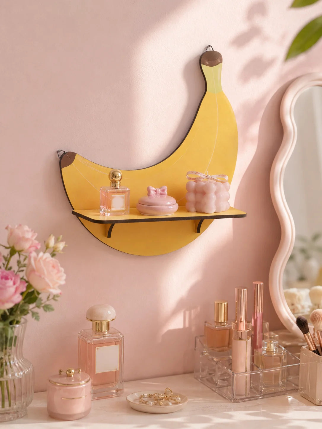 A yellow cherry-shaped wooden wall shelf displaying pink glass perfume bottles and a pink jar on a light pink wall.
