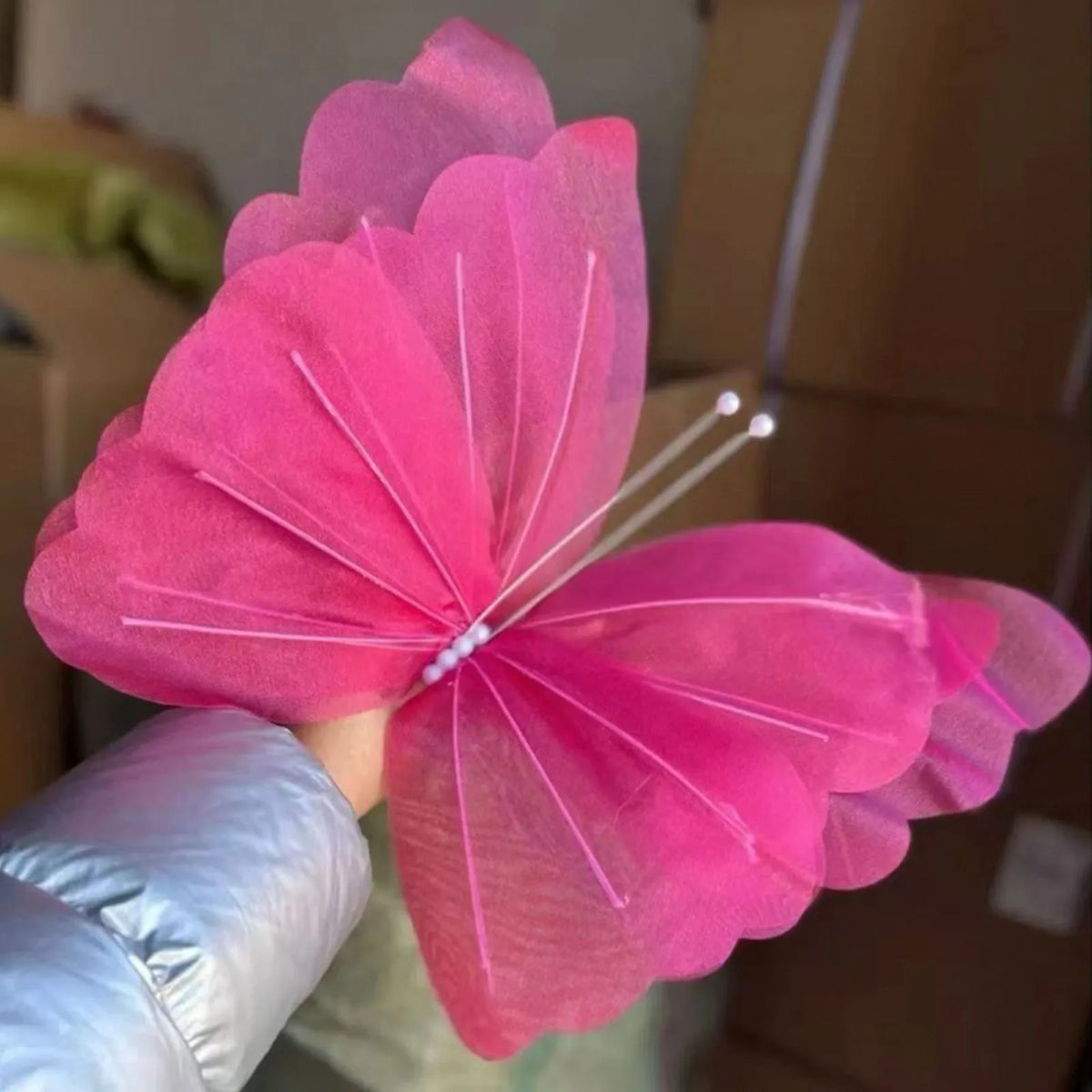A vibrant pink 3D mesh butterfly wall decor is held up against a brown cardboard box.