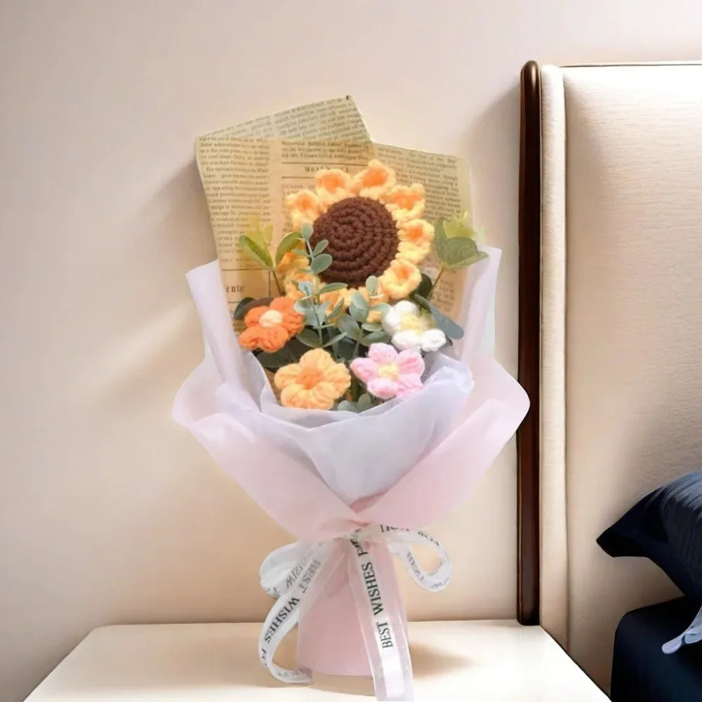 A bouquet of handcrafted crochet sunflowers and daisies wrapped in pink paper and tied with a white ribbon.