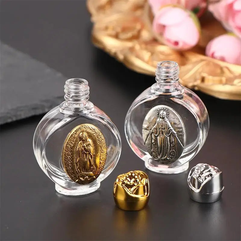 Clear glass bottle with a gold religious sculpture and a small gold charm on a dark surface.