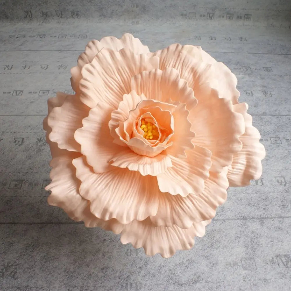 A large, delicate peach colored silk foam rose with layered petals and a central yellow stamen.