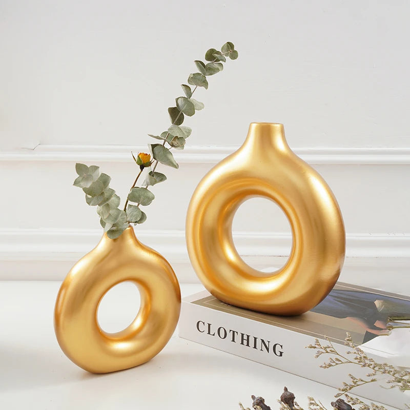 A golden, smooth, ring-shaped resin vase with eucalyptus leaves on a white surface.