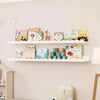 Two white wooden floating shelves display colorful children's books and decorative items.