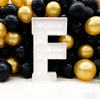 A large white marquee letter F is displayed amidst a pile of gold and black balloons for party decor.