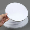 A hand holds a round white corrugated cake board, stacked with several other identical boards.