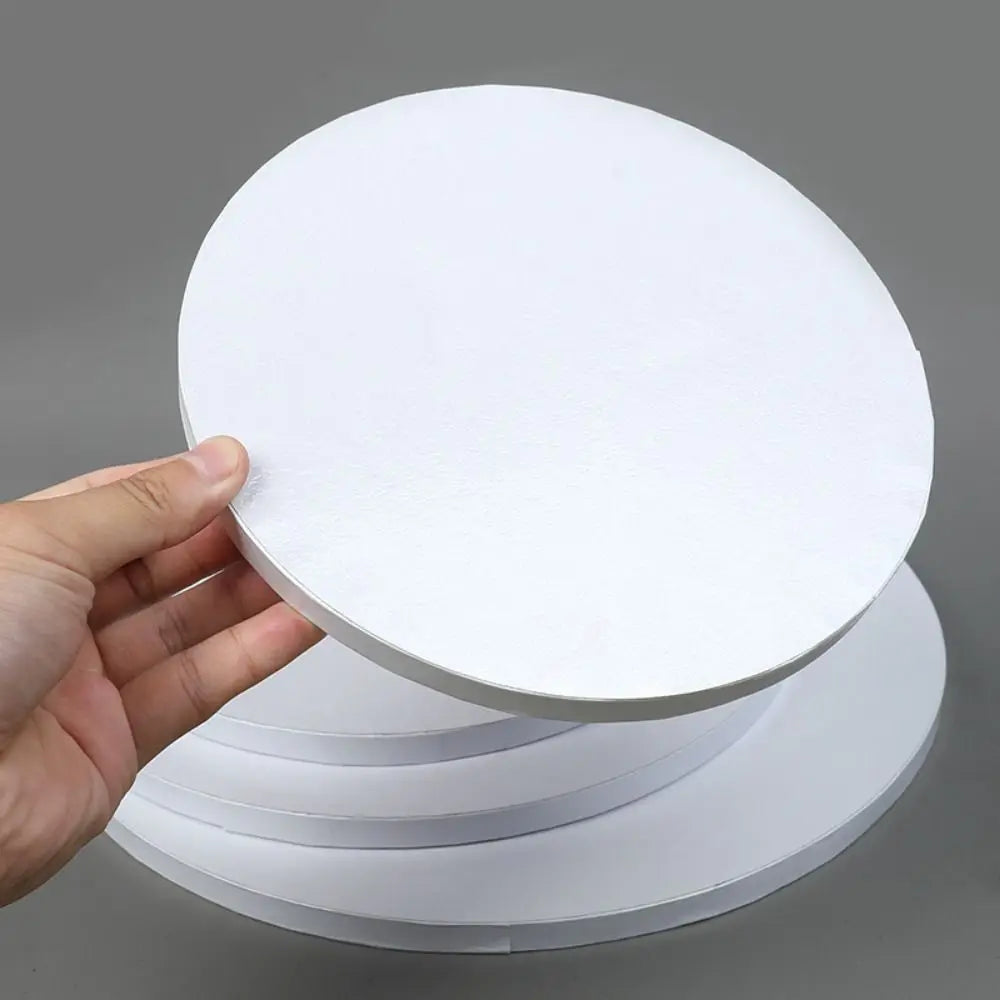 A hand holds a round white corrugated cake board, stacked with several other identical boards.