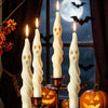 A set of white soy candles shaped like ghosts and mummies displayed in a dark, autumnal Halloween setting.