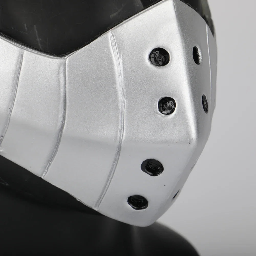A silver cosplay mask with segmented design and small holes is shown on a dark surface.