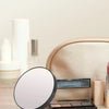 A round magnifying compact mirror with a suction cup and a rectangular makeup palette are shown on a wooden surface.