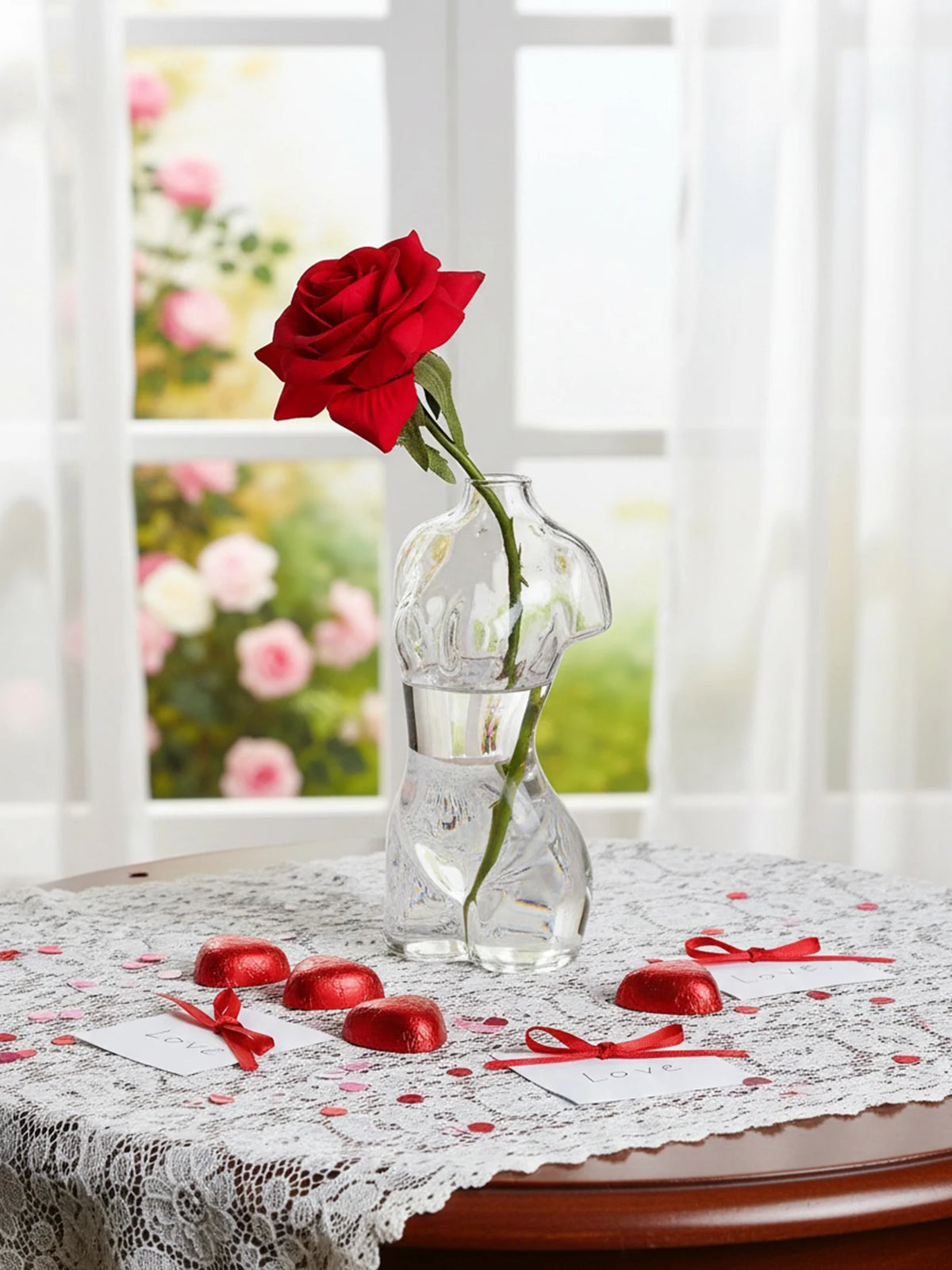 A red rose is placed in an artistic glass human body vase on a lace tablecloth.